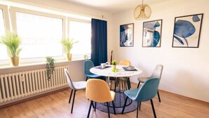 A dining area with a round table, four chairs, and a window with curtains. There are two potted plants on the windowsill and three framed artworks on the wall. - City Loft | 5 Min Rhein-Galerie (Ludwigshafen am Rhein)