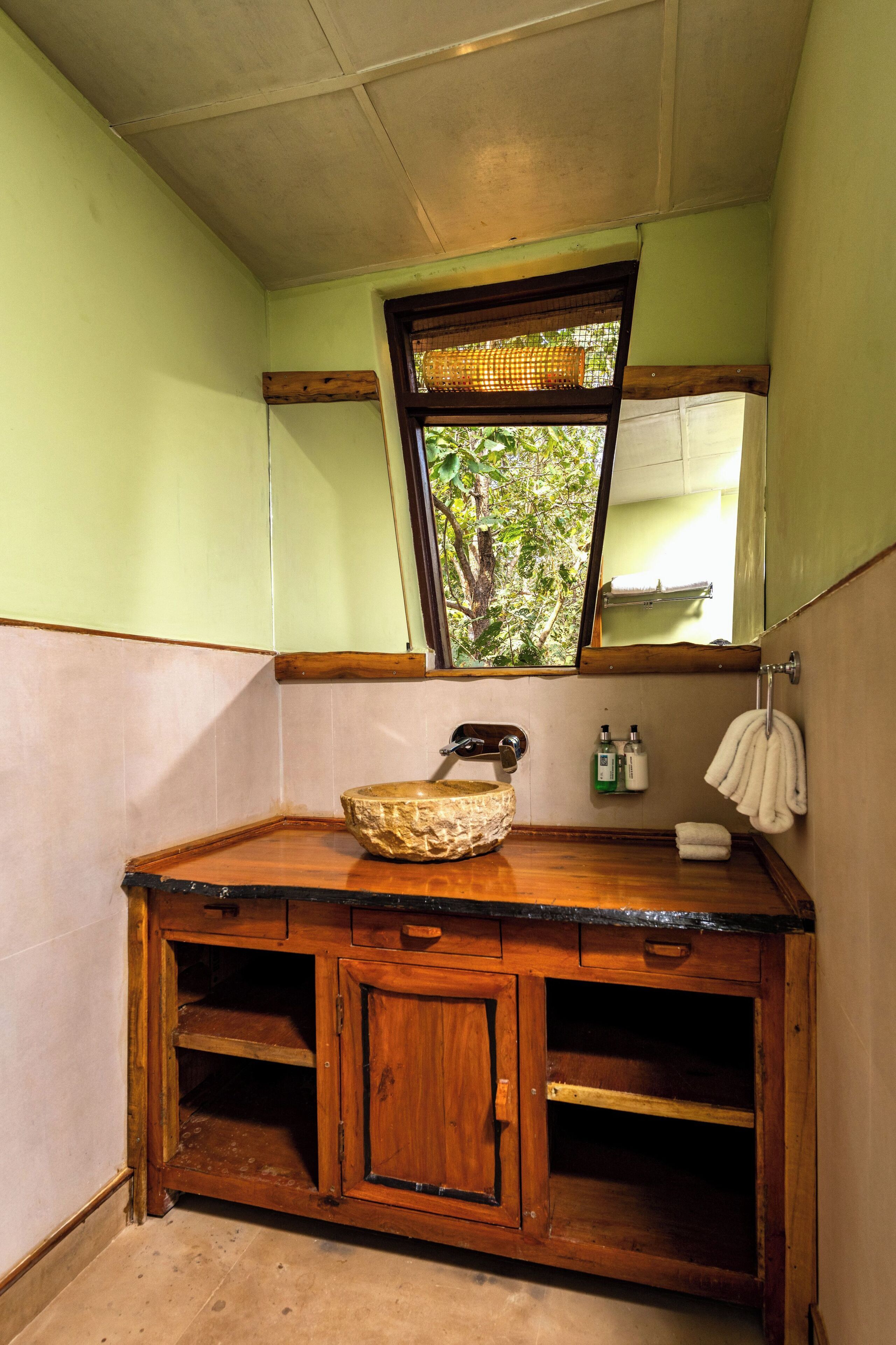 A wooden vanity with a stone basin, a mirror, and a window with a view of greenery.