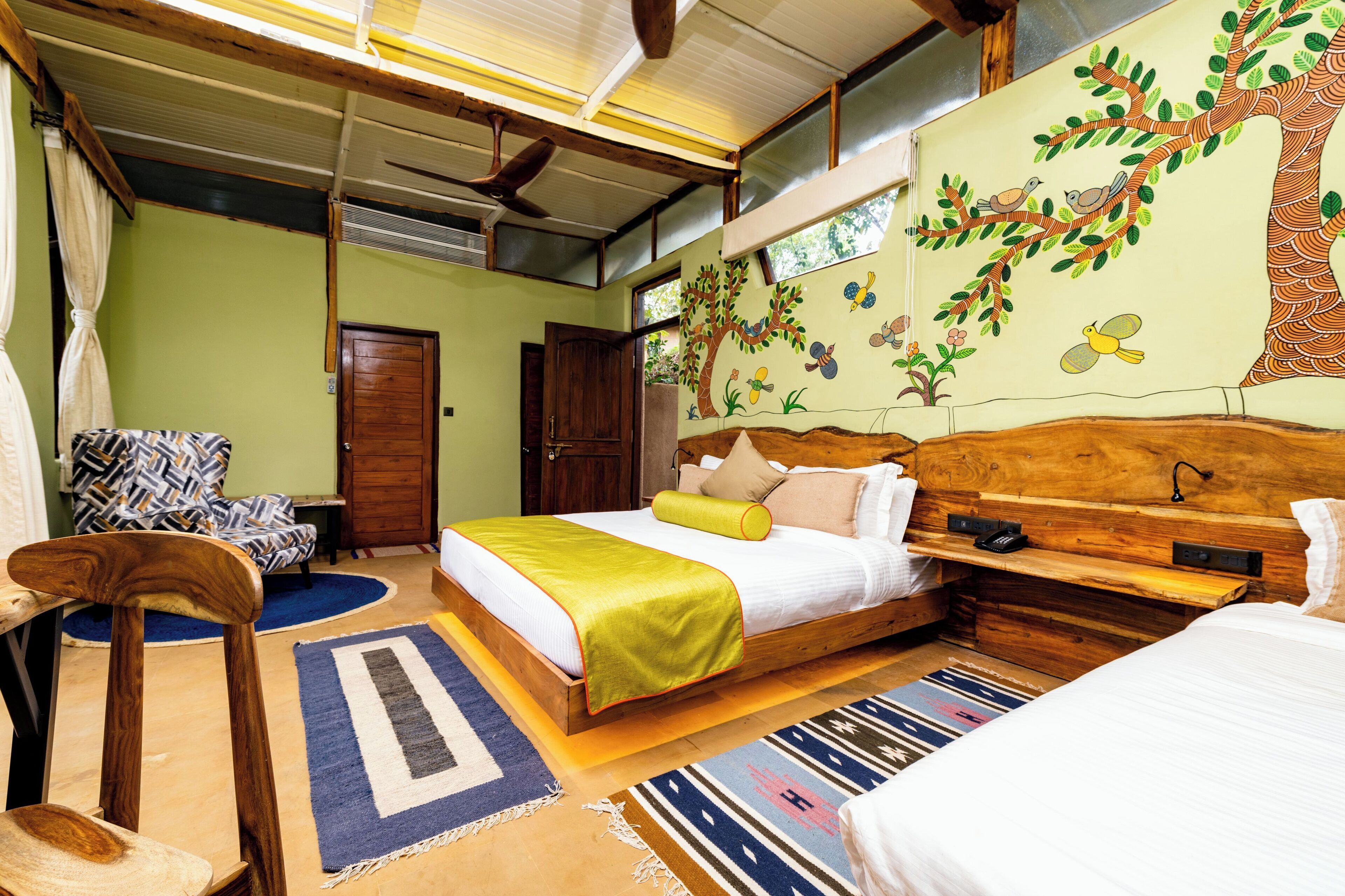 Une chambre à coucher comprenant un lit, une tête de lit en bois, une table de chevet, une chaise et une fresque murale.