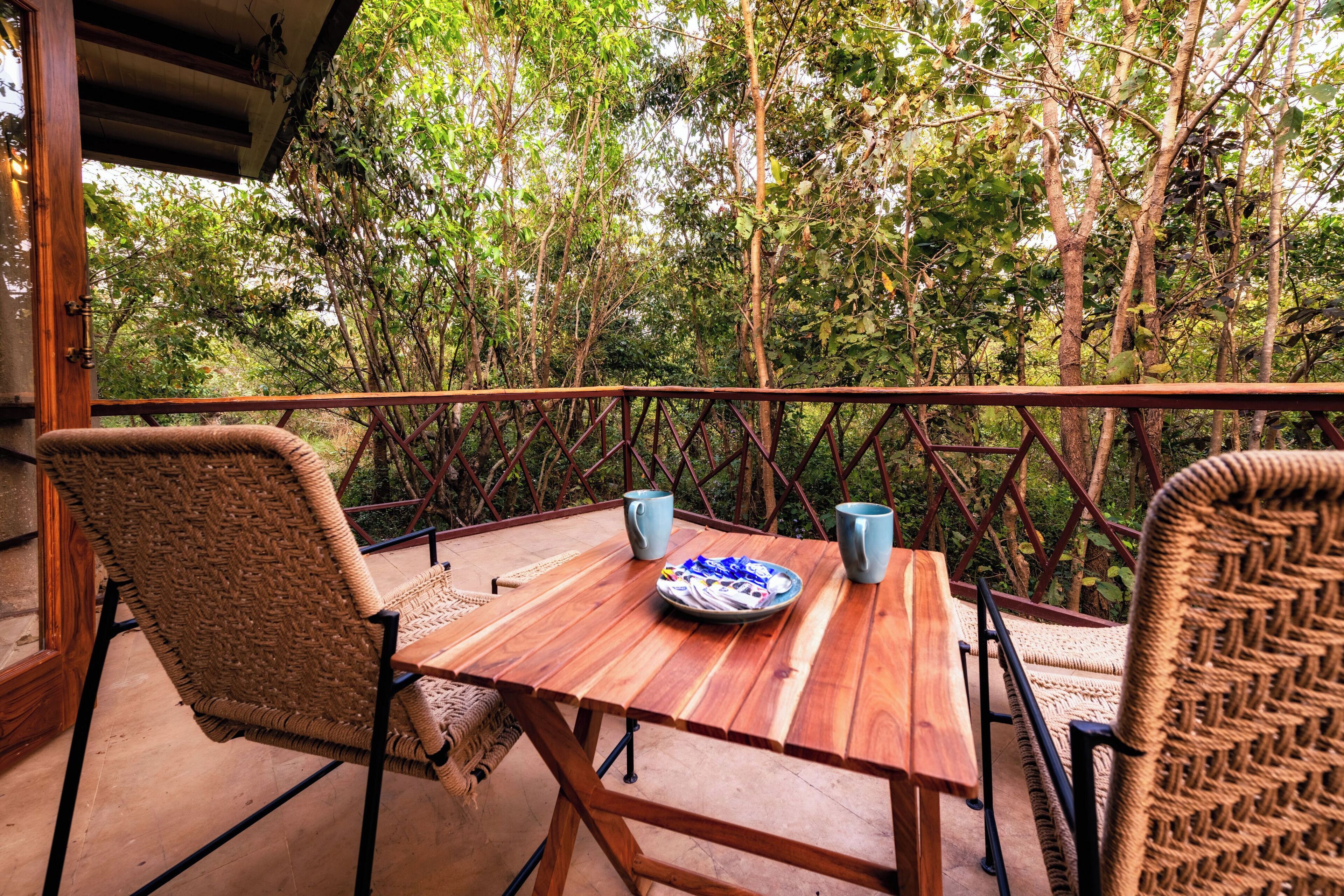 A wooden table with chairs on a balcony, surrounded by lush greenery.