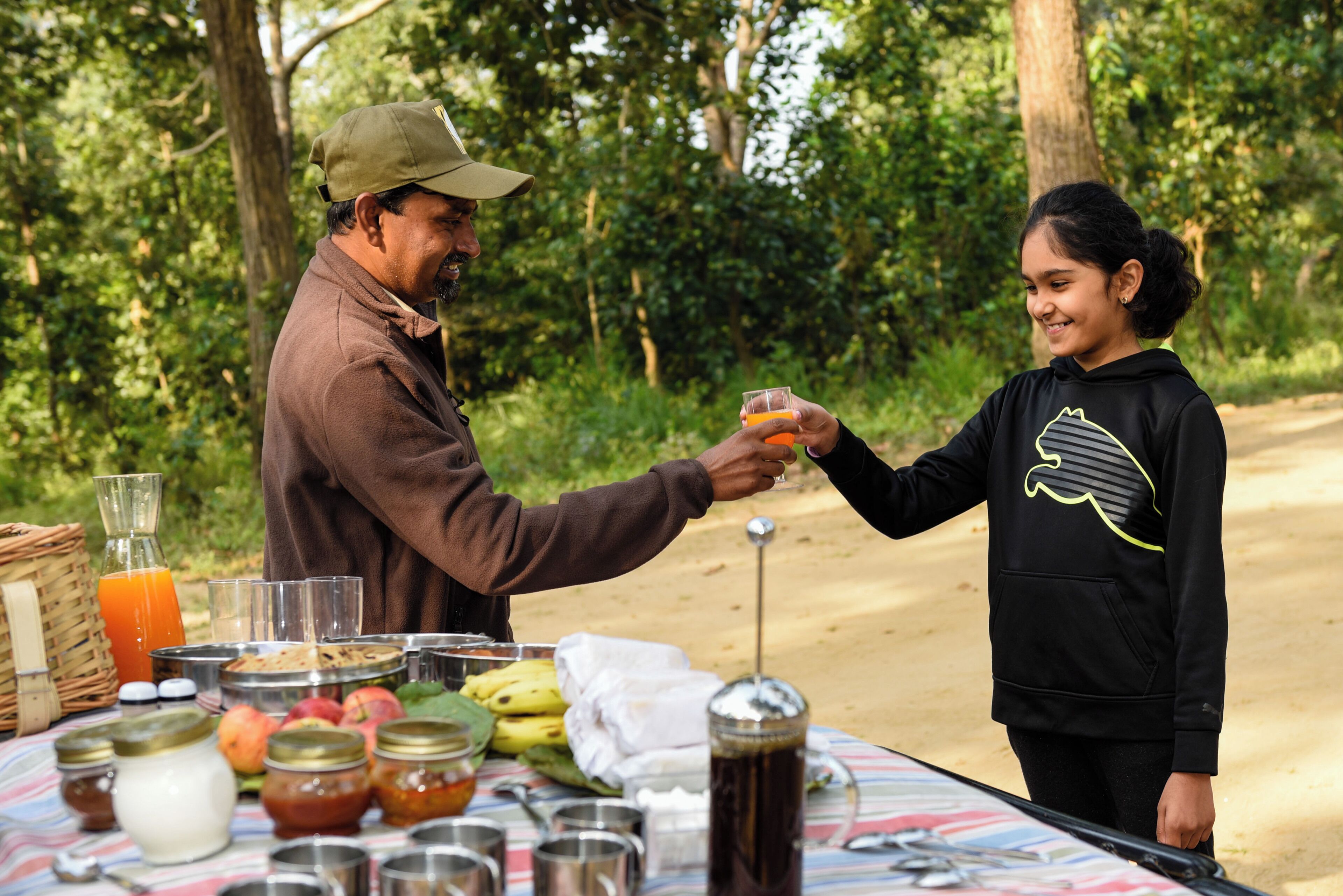 A picnic setup with food and drinks on a table in a wooded area.