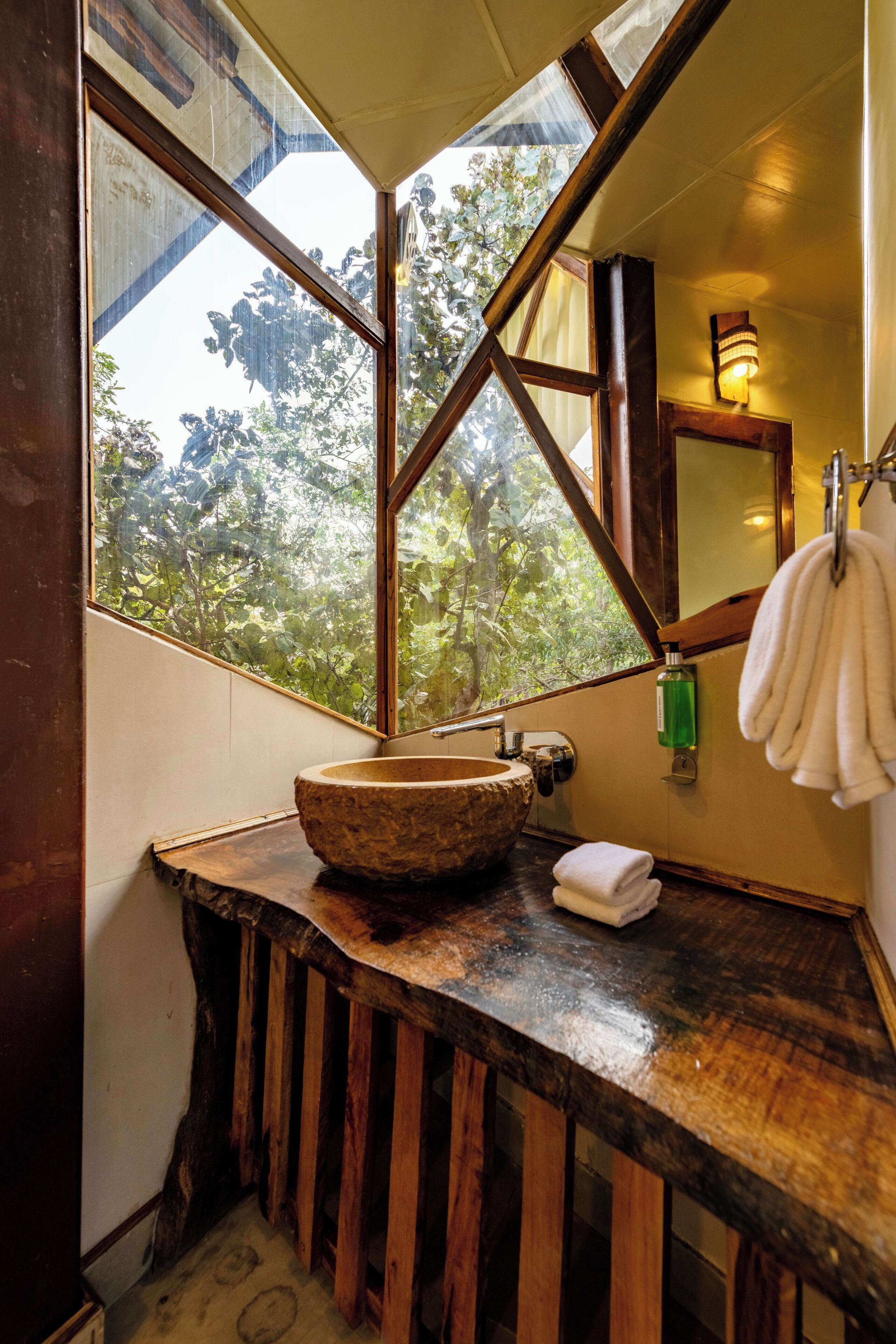A rustic bathroom with a wooden vanity, a large window with a view of trees, and a towel hanging on the wall.