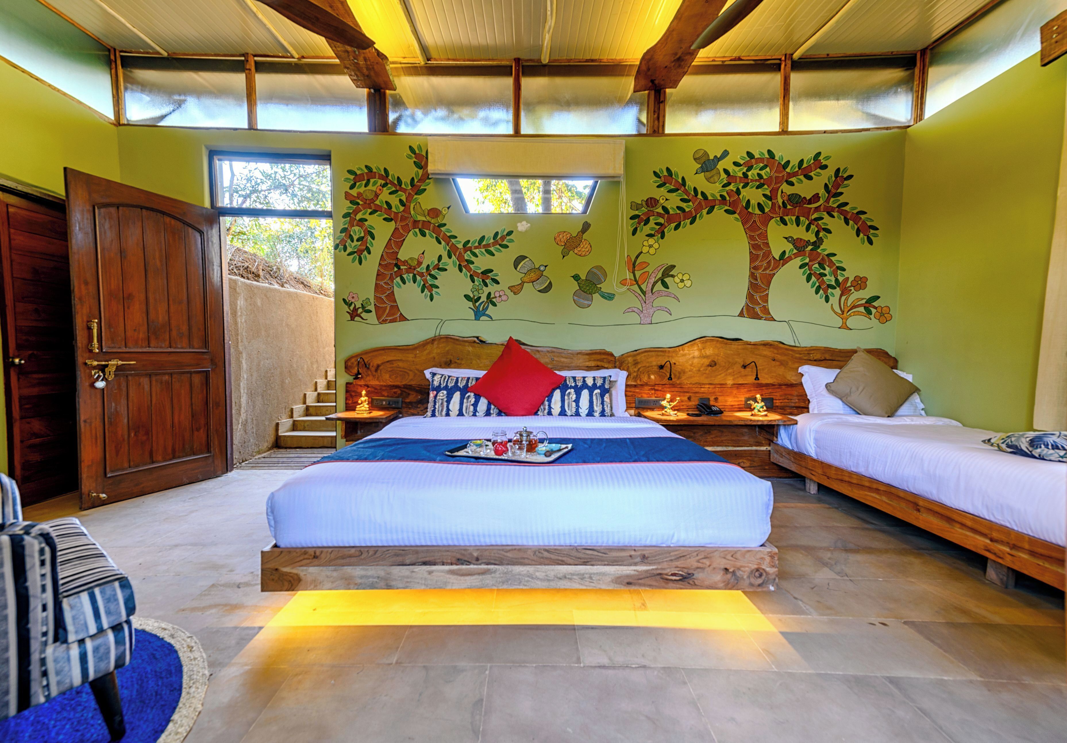 A bedroom with a large bed, two bedside tables, a wooden wardrobe, and a mural of trees on the wall.