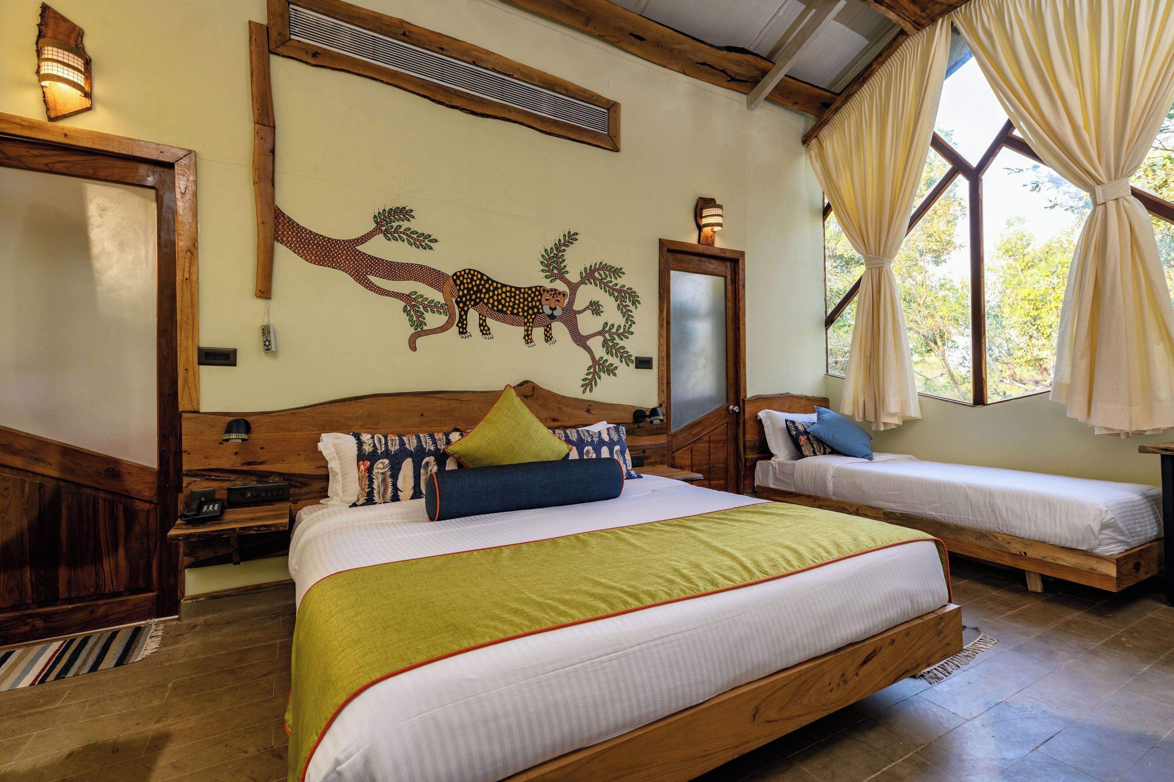 A room with a large bed, a smaller bed, a wooden headboard, a wall mural, and a window with curtains.