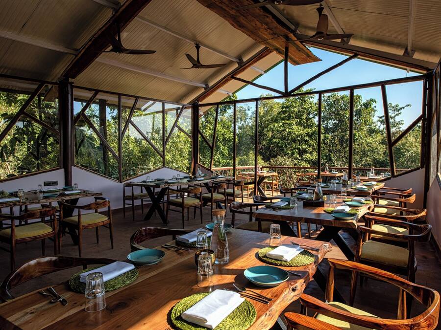 Un área de comedor al aire libre con varias mesas y sillas, ventanas amplias y una estructura de techo de madera.