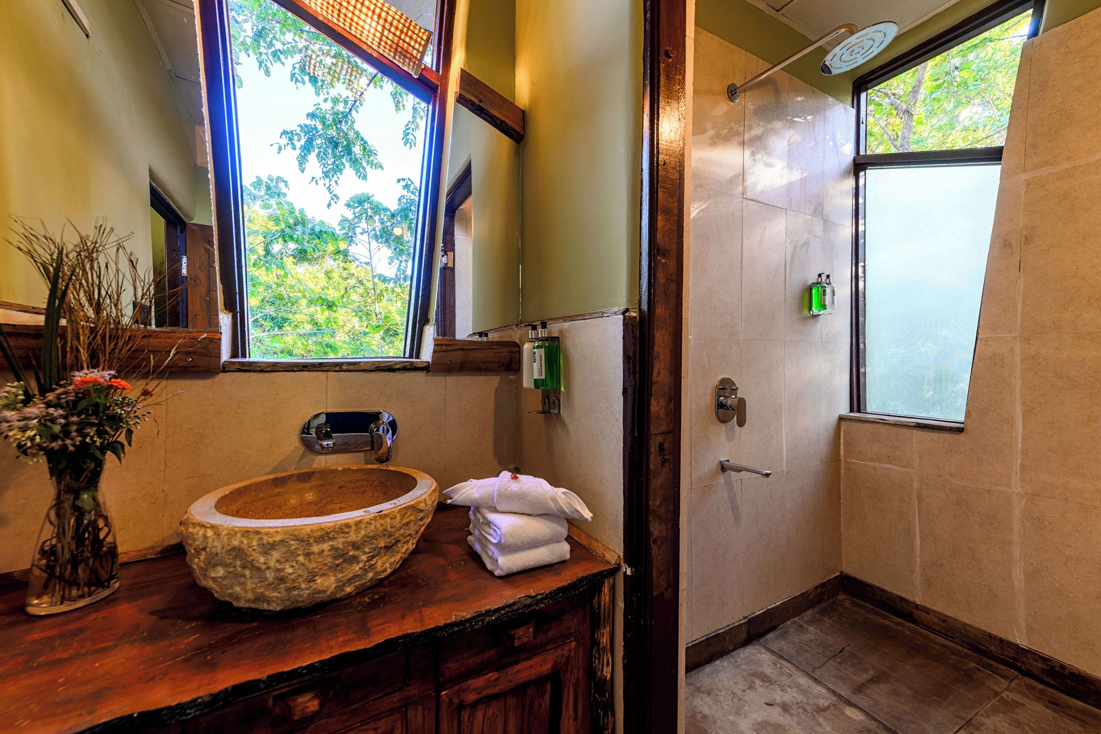 Une salle de bain avec un lavabo en pierre, un miroir, une fenêtre et une douche.
