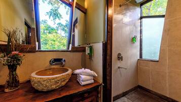 Une salle de bain avec un lavabo en pierre, un miroir, une fenêtre et une douche.