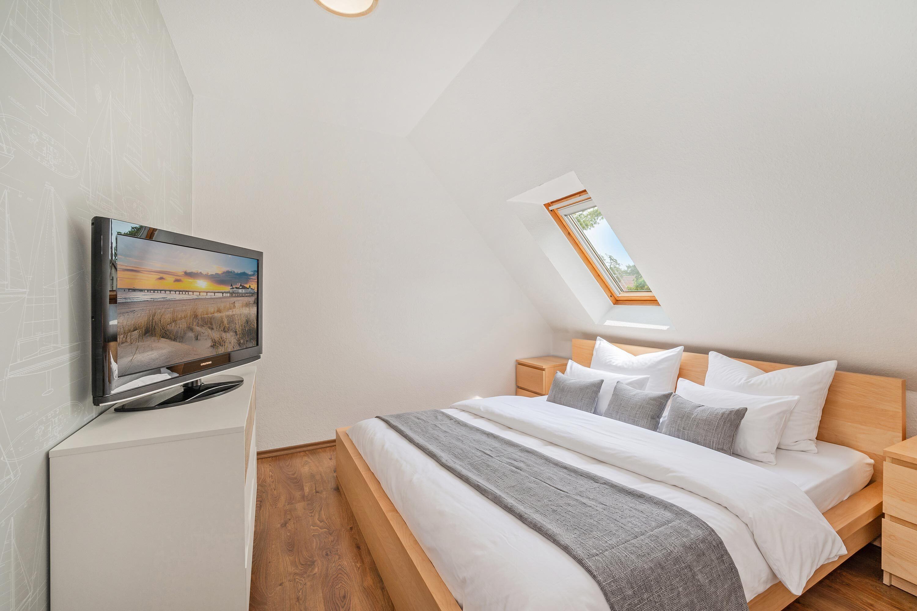 A bedroom with a bed, a television, a skylight, and a wooden nightstand.