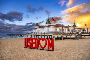A beach with a large red sign reading 'USEDOM' and a building with multiple flags. - Großzügige Ferienwohnung in Ahlbeck in Zentraler Lage für max 4 Personen (Seebad Ahlbeck)