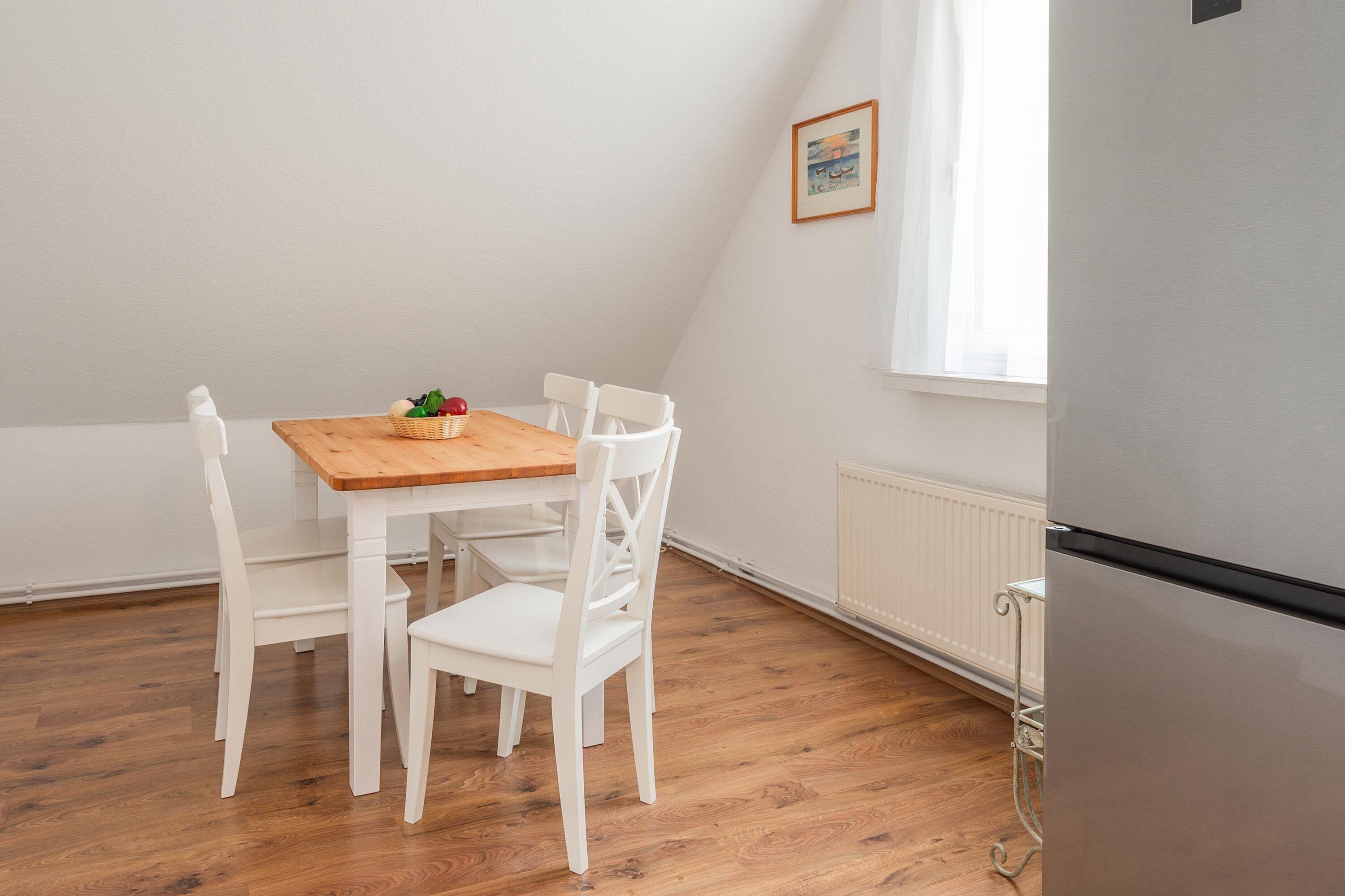 Un petit coin repas avec une table en bois et des chaises blanches, une fenêtre avec des rideaux et un radiateur.