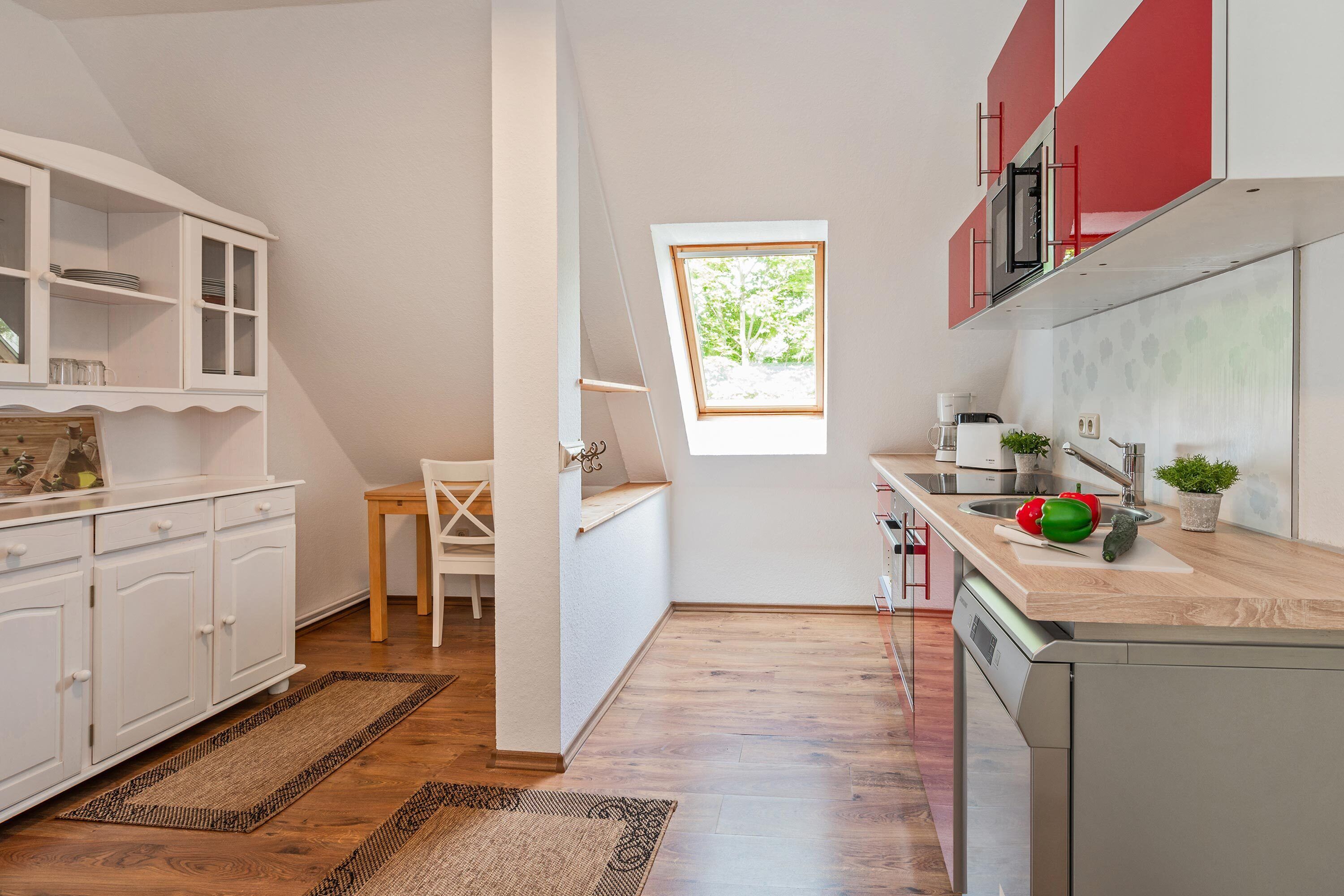 Une cuisine avec des meubles blancs, une table à manger en bois et une fenêtre.