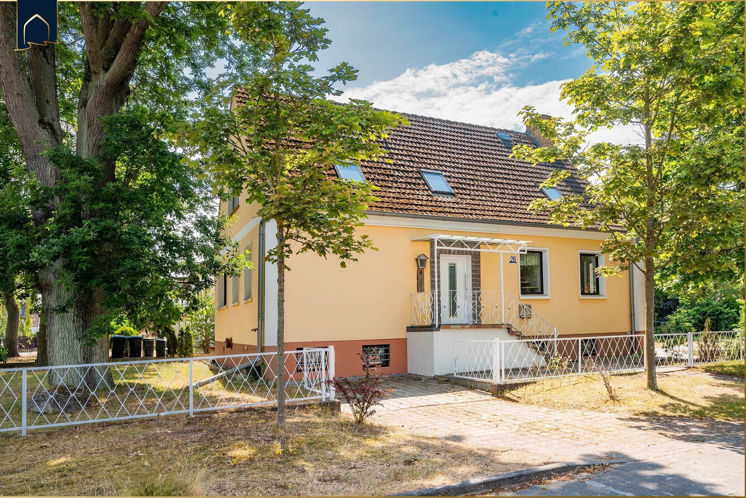 Ein gelbes Gebäude mit einem Ziegeldach, einem weißen Zaun und Bäumen im Vordergrund.