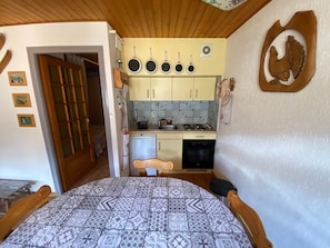 Uma cozinha compacta com área de jantar, apresentando teto de madeira, painel de azulejos e uma pequena geladeira.