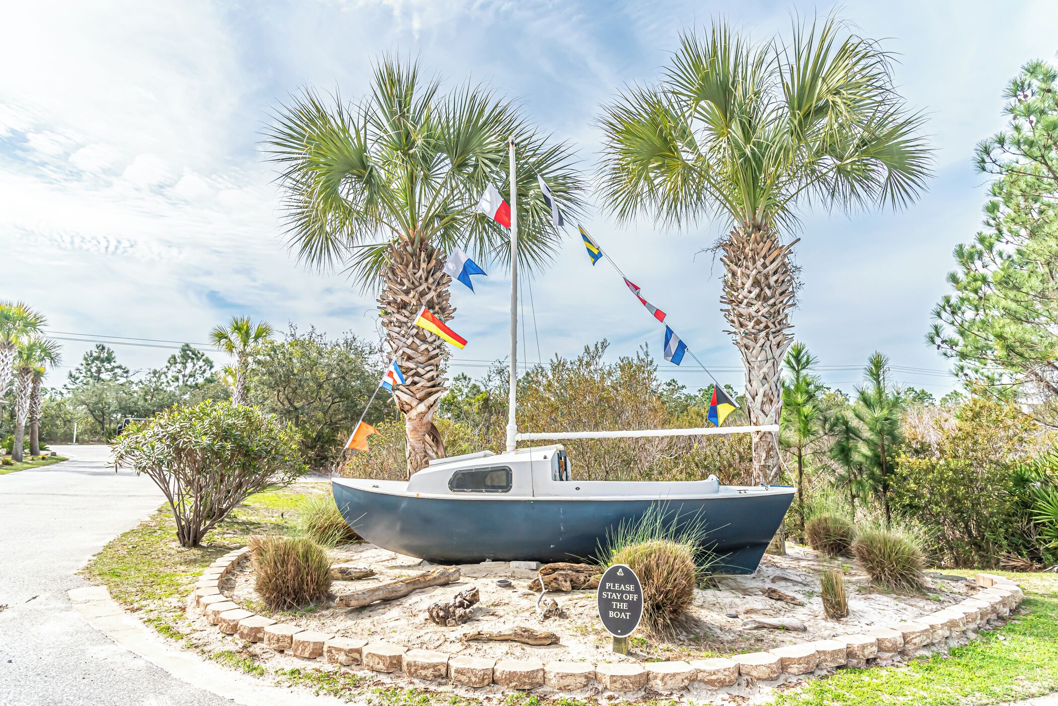 A boat with multiple flags, surrounded by palm trees and a sign that says "PLEASE STAY OFF THE BOAT."