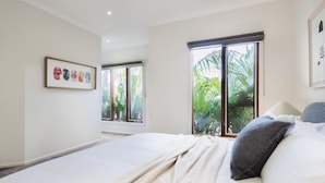 Un dormitorio con cama, ventana con vista a follaje y una obra de arte enmarcada en la pared.