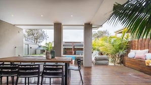 Un patio amplio con mesa y sillas de madera, una piscina al fondo y una terraza de madera.