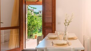 A dining area with a table set for four, a wooden door leading outside, and a small garden visible through the door. - Outstanding Residenze Gallura 1 Bedroom Sleeps 4 Persons Plus Child bed Possible (San Teodoro)