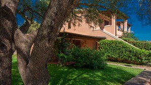 A house with a stone pathway leading to a wooden door, surrounded by lush greenery and trees. - Outstanding Residenze Gallura 1 Bedroom Sleeps 4 Persons Plus Child bed Possible (San Teodoro)