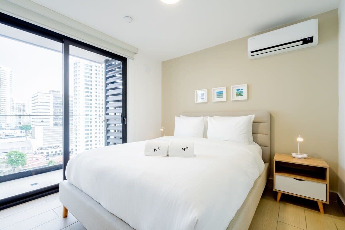 Une chambre d’hôtel moderne dotée d’un grand lit, d’une table de chevet, d’un climatiseur fixé au mur et offrant une vue sur la ville grâce à une grande fenêtre.