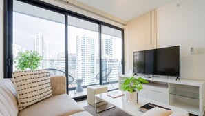 A modern living room with a large TV, comfortable seating, a coffee table, and a city view through large windows.