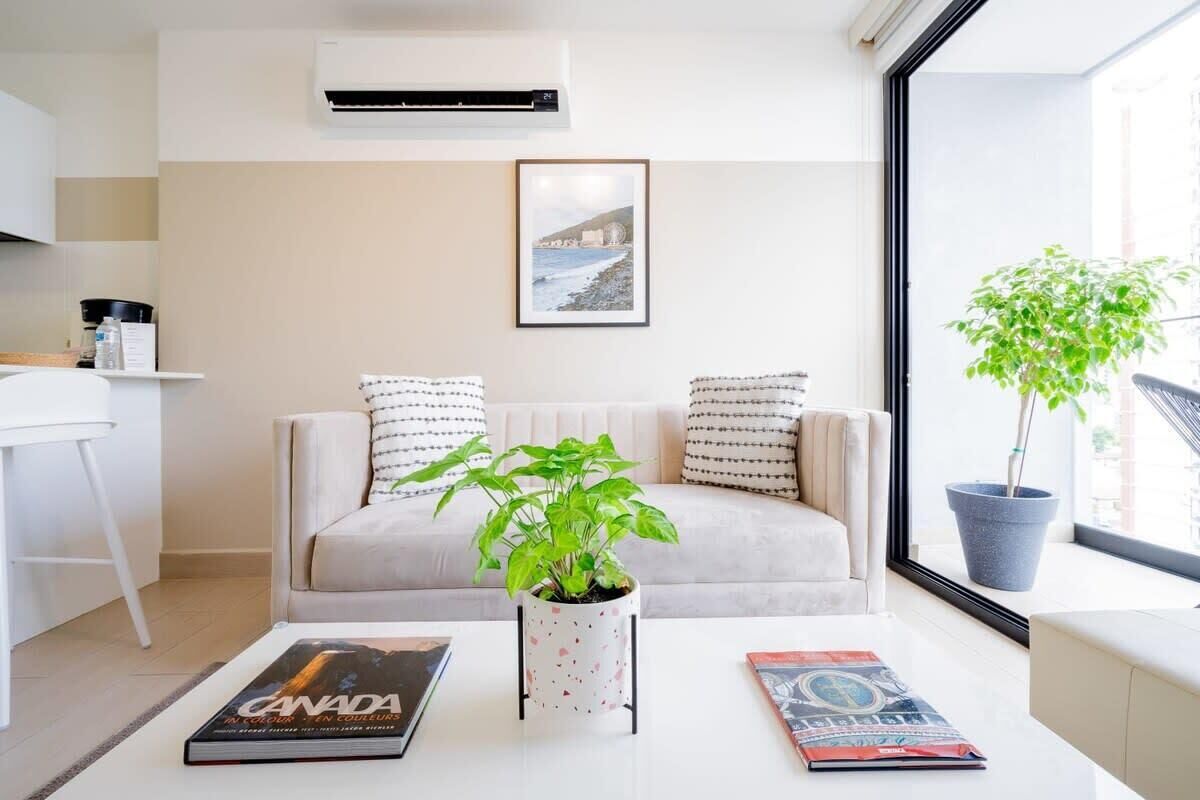 Una sala de estar moderna con un sofá color beige, una mesa de centro con una planta en maceta y un cuadro enmarcado en la pared.
