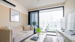 A modern living room with a sofa, coffee table, and a large window offering a city view.