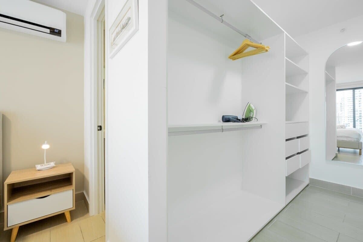 A modern, white room with built-in storage, a small bedside table, and a hanging rack.
