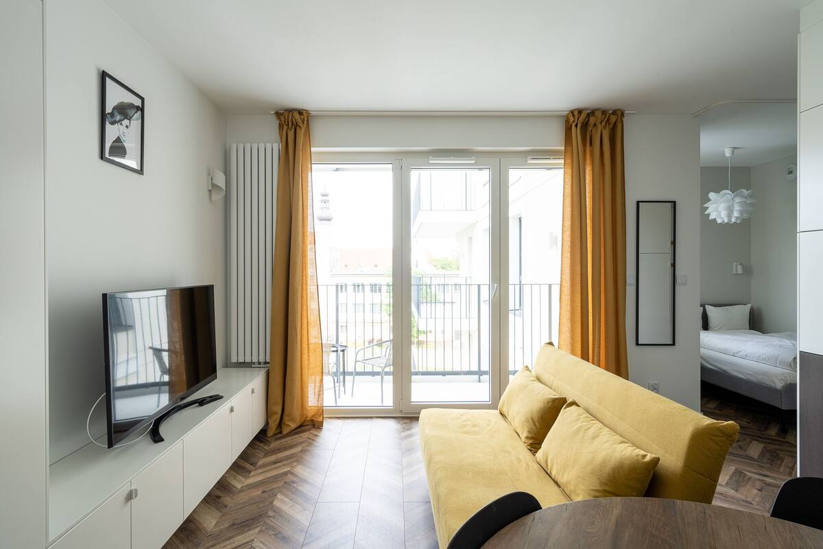 A modern living room with a sofa, TV, and a balcony with curtains.