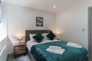 A hotel room with a bed, two pillows, a nightstand with a lamp, and a painting on the wall. - Central Preston Contemporary 1 Bedroom Apartment (Preston)