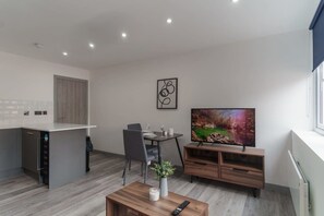 A modern kitchen with a dining area, a flat-screen TV, and a small coffee table. - Central Preston Contemporary 1 Bedroom Apartment (Preston)