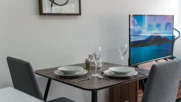 A dining area with a table set for two, a television displaying a scenic landscape, and a framed abstract artwork on the wall.