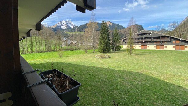 A view from a balcony overlooking a grassy field with a building and mountains in the background.