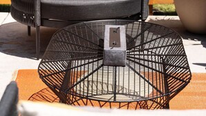 A wicker chair with grey cushions, a metal table with a rectangular object on it, and a potted plant. - Modern Guest House Near Downtown! (Washougal)
