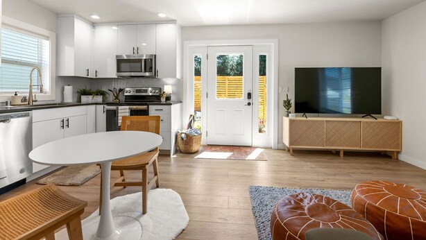 A modern kitchen with white cabinets, a dining area with a white table and chairs, a TV, and a wicker basket. - Modern Guest House Near Downtown! (Washougal)