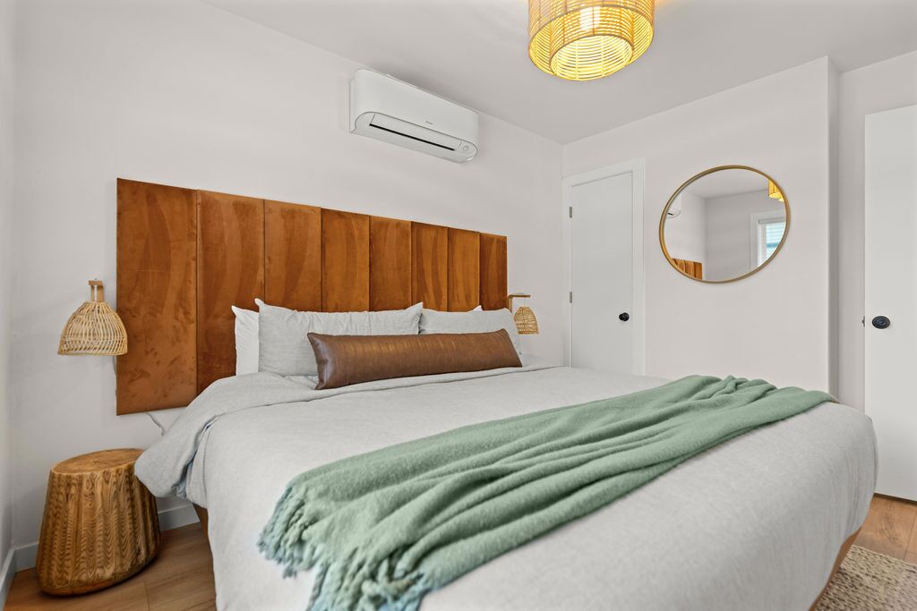 Ein Schlafzimmer mit einem hölzernen Kopfteil, einem runden Spiegel, einer grünen Tagesdecke und einer Lampenschirm aus Weidengeflecht.