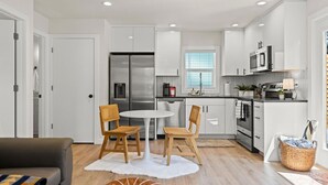 A modern kitchen with white cabinets, stainless steel appliances, and a dining area with a white table and wooden chairs. - Modern Guest House Near Downtown! (Washougal)