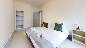 Une chambre d’hôtel avec deux lits, une table de chevet avec une lampe, une armoire et une étagère.