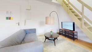 A living room with a sofa, a coffee table with a vase, a TV on a stand, and a staircase.