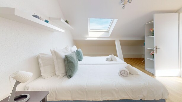 A bedroom with a skylight, a bed with pillows, a bedside table, and a wardrobe.