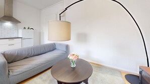 A modern living room with a grey sofa, a round wooden coffee table with a vase of flowers, and a large floor lamp.