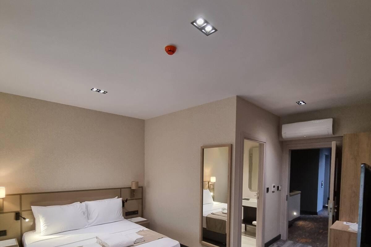 Una habitación de hotel con una cama grande, mesitas de noche, una mesa redonda de madera y un espejo.