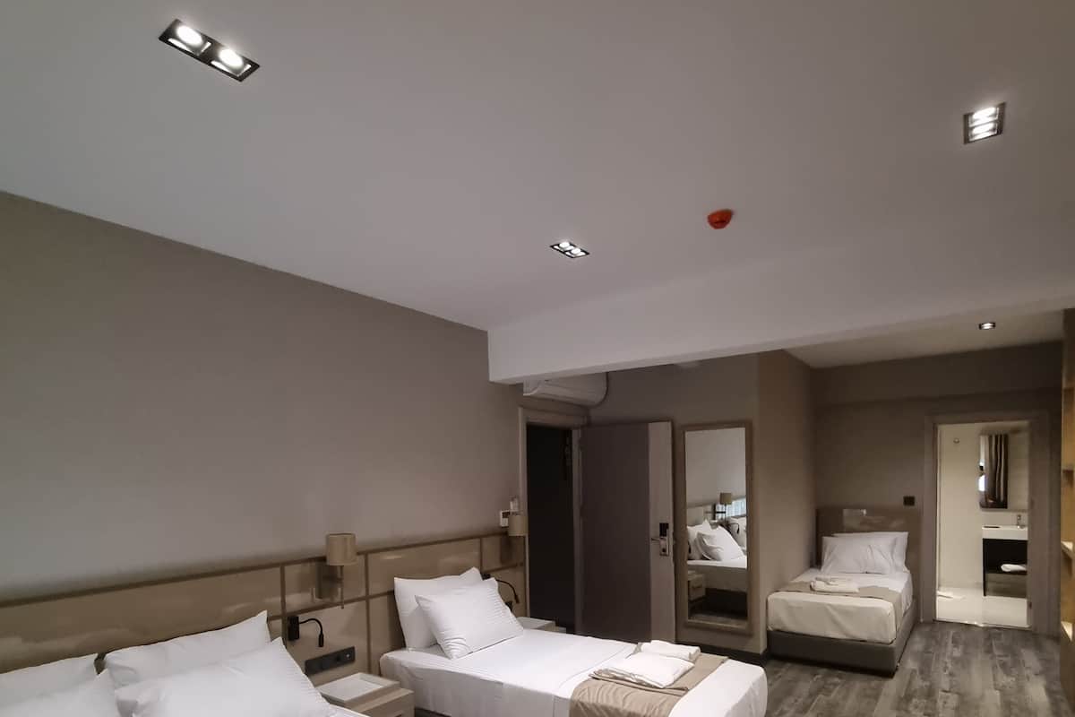 Habitación de hotel con dos camas, un sofá y un baño visible a través de una puerta abierta.