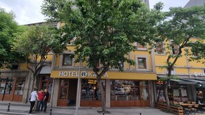 Un hôtel à la façade jaune, avec un grand arbre devant.