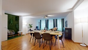 Ein moderner Essbereich mit einem Holztisch, gedeckt für vier Personen, umgeben von Stühlen. Eine kleine Seitentisch mit einer Lampe ist links sichtbar.