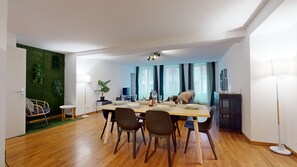 Ein moderner Essbereich mit einem Holztisch, gedeckt für vier Personen, umgeben von Stühlen. Eine kleine Seitentisch mit einer Lampe ist links sichtbar.
