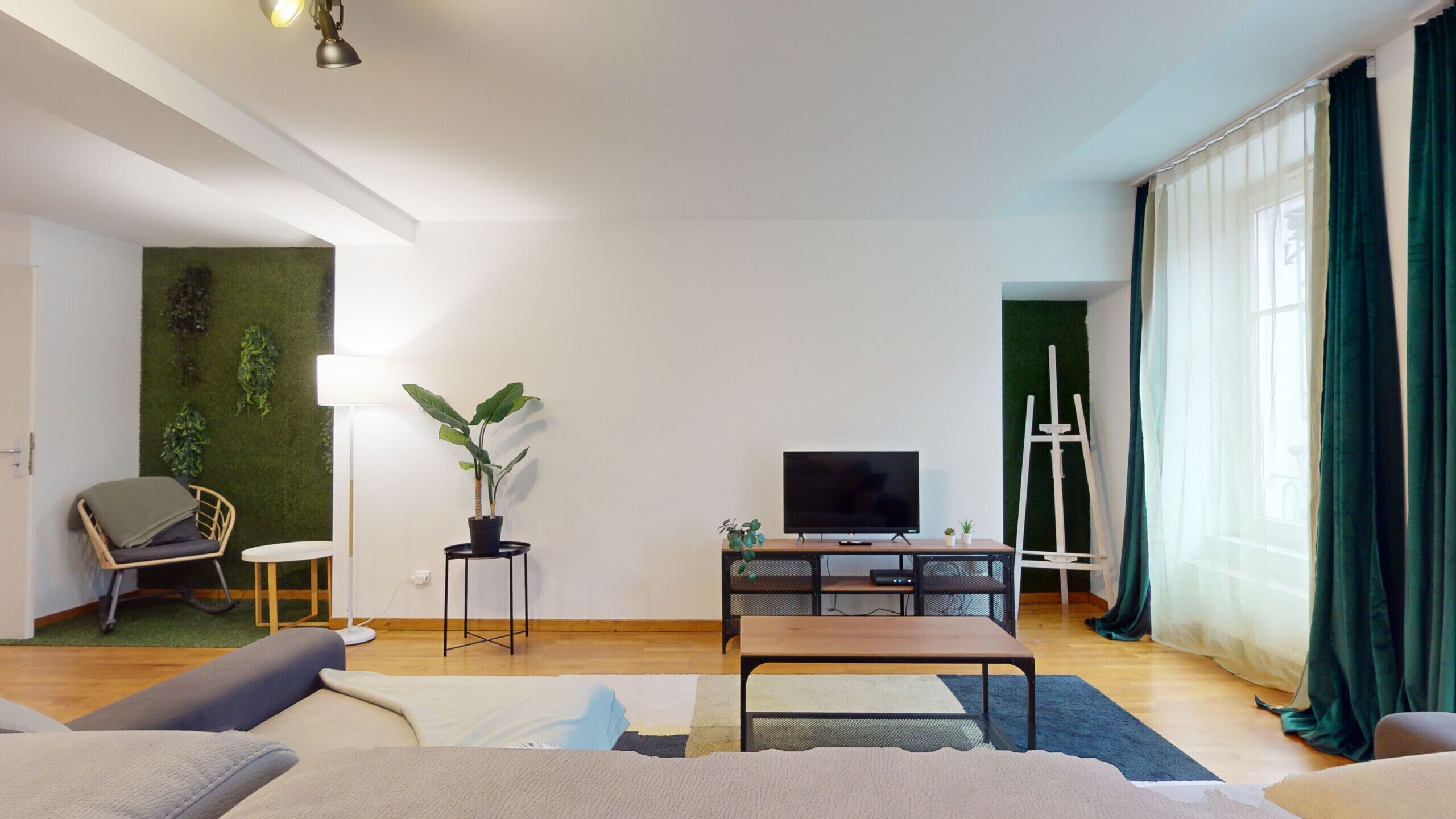 A modern living room with a flat-screen TV, a wooden coffee table, a sofa, a small side table, and a potted plant.