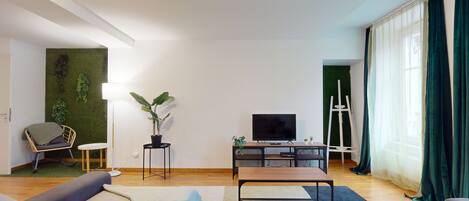 A modern living room with a flat-screen TV, a wooden coffee table, a sofa, a small side table, and a potted plant.