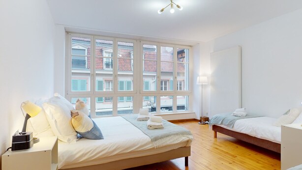 Ein Hotelzimmer mit großem Fenster, zwei Betten, einem Nachttisch mit Lampe und einer Heizung.