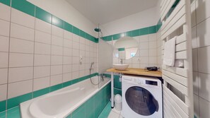A modern bathroom with a bathtub, a sink, a mirror, and a washing machine.