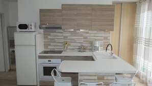 A modern kitchen with a microwave, oven, and sink. There are two white chairs and a small table. - Appartement Neuf Bages Avec Balcon (Bages)